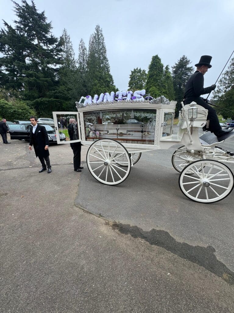 Horse-drawn carriage with floral decorations at a funeral service.