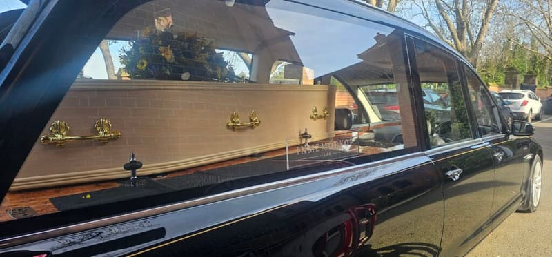 Coffin inside a hearse parked outside with floral arrangement.